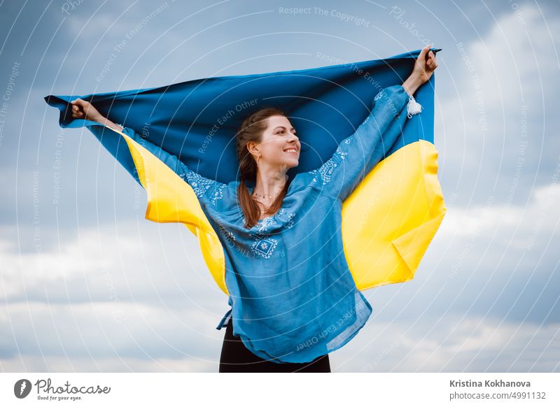 Glückliche freie ukrainische Frau mit Nationalflagge auf dramatischen Himmel Hintergrund. Porträt der Dame in blauer Stickerei vyshyvanka Shirt. Ukraine, Unabhängigkeit, patriotisches Symbol