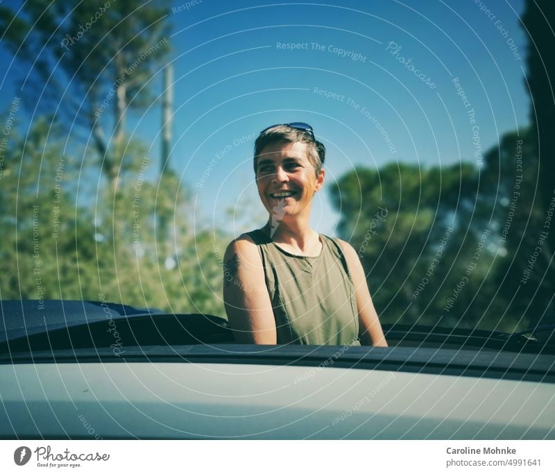 Frau schaut lachend aus einem Autodach heraus glücklich lächeln Porträt schoen hübsch Lifestyle Erholung Urlaub Reise freizeit Sonne Natur Sommer freiheit