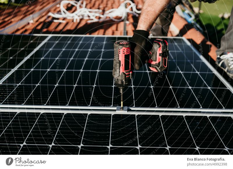 Hand von reifen Techniker Mann Montage von Sonnenkollektoren mit Bohrer auf Hausdach für Selbstverbrauch Energie. Erneuerbare Energien und grünes Energiekonzept