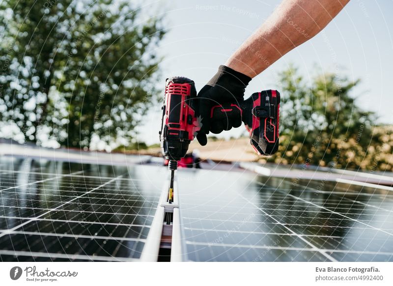 close up Hand von reifen Techniker Mann Montage von Sonnenkollektoren mit Bohrer auf Hausdach für Selbstverbrauch Energie. Erneuerbare Energien und grünes Energiekonzept