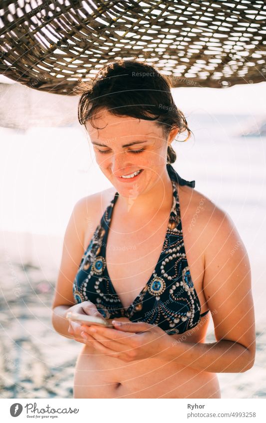 Junge kaukasische Frau Frau verwenden Smartphone unter Strand Sonnenschirm auf Sonnenuntergang. Urlaub am Meer Ozean aktiver Lebensstil attraktiv authentisch