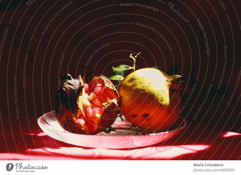 Vertikale Aufnahme von Licht und Schatten, die auf zwei Granatapfelfrüchte in einer Glasplatte geworfen werden, die einen herbstlichen Hintergrund und Ästhetik zeigt