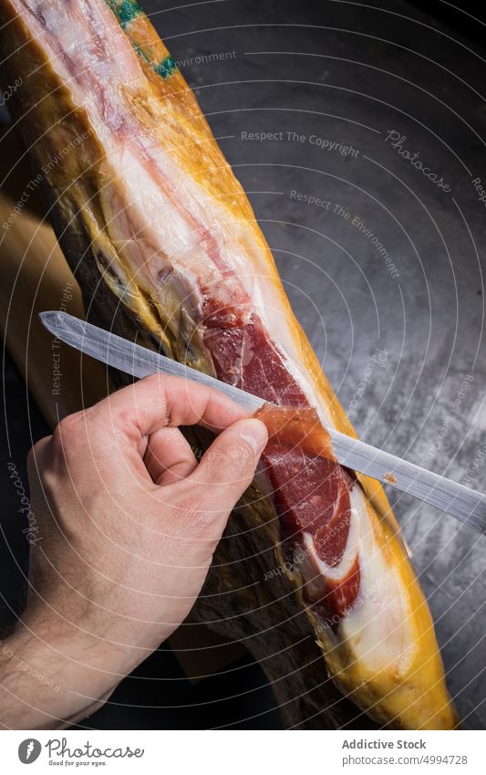 Gesichtsloser Koch schneidet köstliche Schinkenkeule mit Messer Küchenchef geschnitten Jamón Schweinefleisch Delikatesse Fleisch Protein Scheibe geschmackvoll