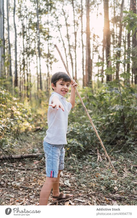 Lächelnder Junge mit Zweig im Sommerwald ausdehnen Kindheit herzlich freundlich Wald Natur Porträt Jeansstoff Shorts T-Shirt Wälder Inhalt charmant angenehm