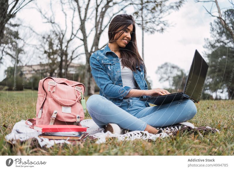 Glückliche Frau mit Laptop im Park Schüler benutzend Bildung Prüfungsvorbereitung lernen online Campus jung ethnisch hispanisch Jeansstoff Jeanshose Hausaufgabe