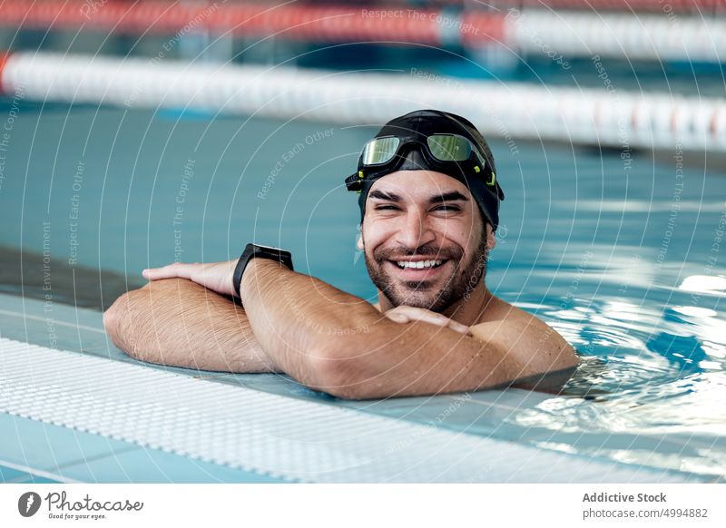 Lächelnder Schwimmer mit Schwimmbrille, der sich an den Beckenrand lehnt sich auf die Hand lehnen herzlich Schutzbrille freundlich maskulin Mann Porträt Athlet