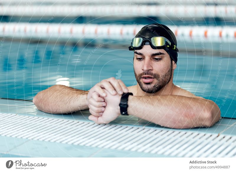 Schwimmer mit Schwimmbrille, der im Schwimmbad die Zeit auf seiner Armbanduhr überprüft prüfen Schutzbrille maskulin Macho Pool Mann Porträt Accessoire achtsam