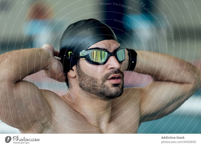 Muskulöser Schwimmer mit Schwimmbrille und Kappe am Pool Athlet Schutzbrille Hand hinter dem Kopf Bizeps sportlich maskulin Macho Mann Porträt brutal Trizeps