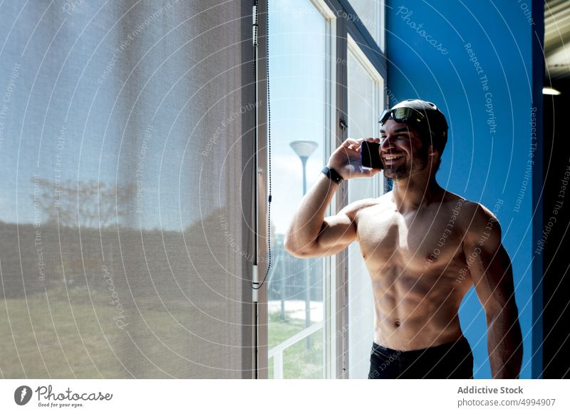 Fröhlicher Schwimmer, der mit seinem Smartphone gegen ein Fenster spricht reden nackter Torso Sixpack muskulös Lächeln Mann