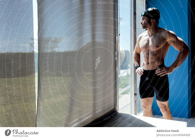 Muskulöser Schwimmer mit nacktem Oberkörper hinter einem Fenster im Sonnenlicht Athlet nackter Torso Sixpack Bauchmuskeln verträumt Macho maskulin Körper Mann