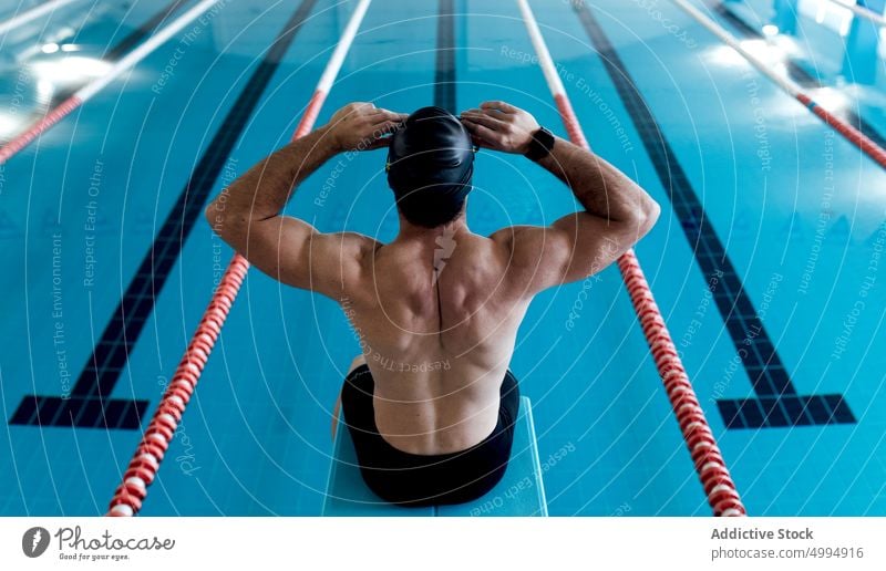 Nicht erkennbarer muskulöser Sportler, der auf einem Block am Pool sitzt Training Schwimmsport Klotz Mann Schwimmer Podest vorbereiten professionell