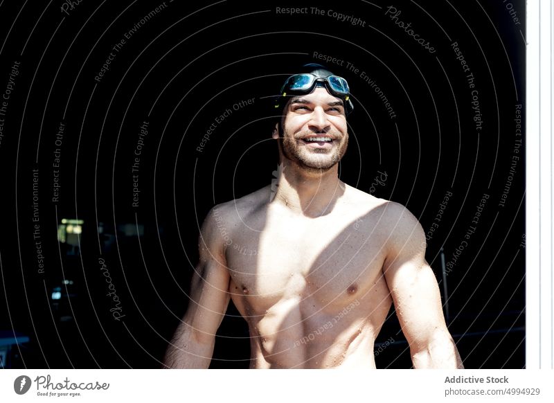 Glücklicher muskulöser Schwimmer mit nacktem Oberkörper hinter einem Fenster im Sonnenlicht Athlet nackter Torso Sixpack Bauchmuskeln verträumt Macho maskulin