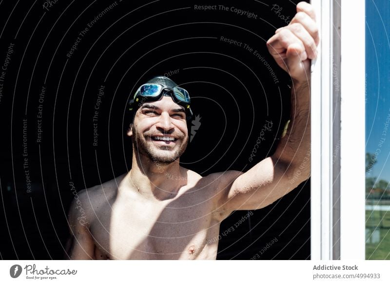 Glücklicher muskulöser Schwimmer mit nacktem Oberkörper hinter einem Fenster im Sonnenlicht Athlet nackter Torso Sixpack Bauchmuskeln verträumt Macho maskulin