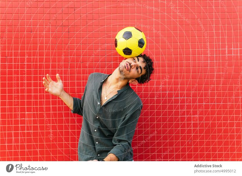 Hispanischer Mann macht Trick mit Fußball Gleichgewicht Ball Straße Wand farbenfroh hell Wochenende männlich jung hispanisch ethnisch jonglieren urban Energie
