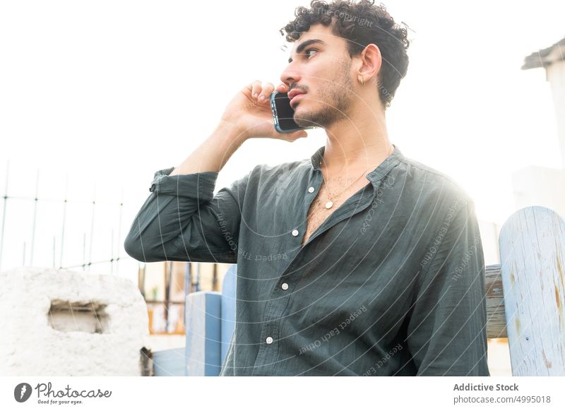 Hispanischer Mann spricht mit Smartphone vor dem Haus benutzend Telefonanruf fettarm Zaun soziale Netzwerke Straße Wochenende männlich jung zuhören sprechen