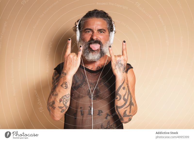 Bärtiger Mann zeigt Rock-Geste und hört Musik Rocker Felsen gestikulieren auflehnen zuhören ausspannen Rock and Roll Hupe männlich reif Mittelfinger grauer Bart