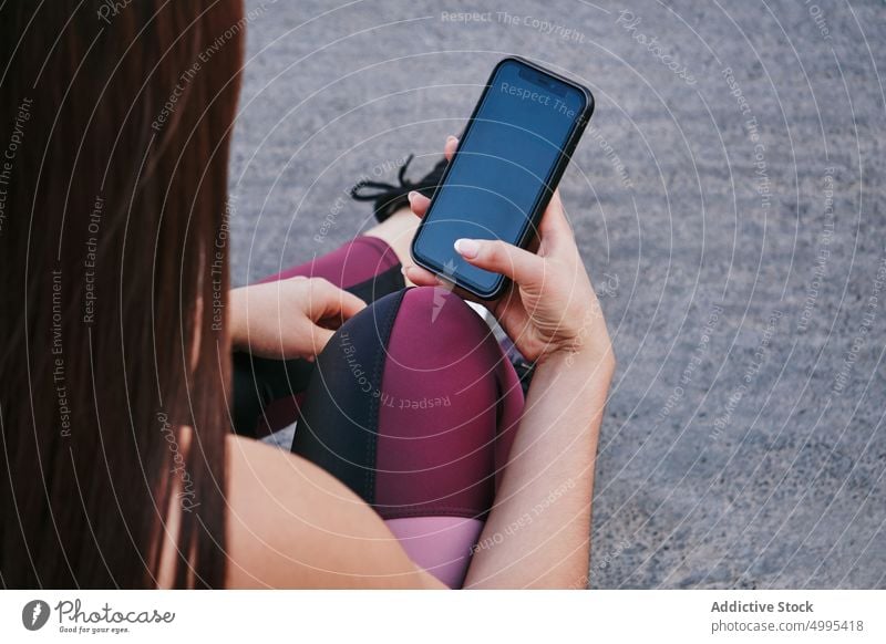 Crop-Sportlerin mit Smartphone auf der Straße benutzend Pause Training Fitness soziale Netzwerke online Boden Frau Athlet sitzen Mobile Telefon
