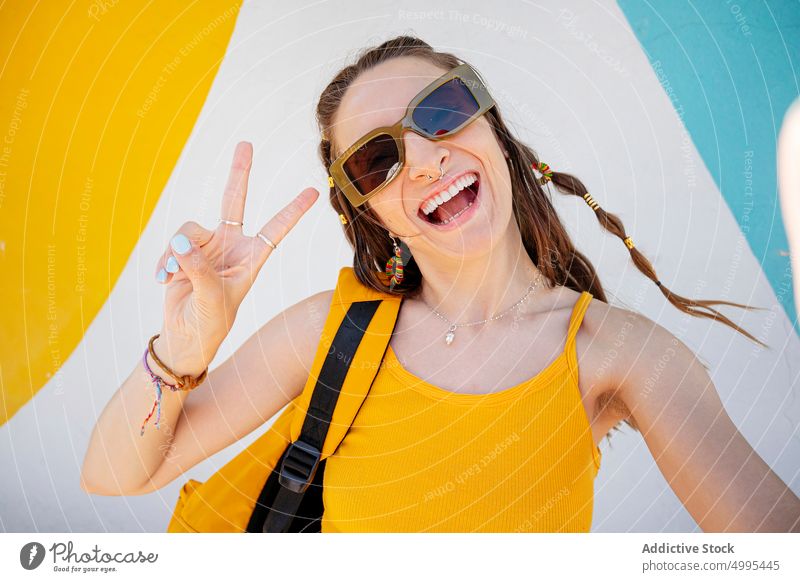Glückliche Frau nimmt Selfie auf der Straße lustig modern urban v-Zeichen zwei Finger Sonnenbrille Grimasse Stil jung Brille heiter Rucksack Gedächtnis Tourist