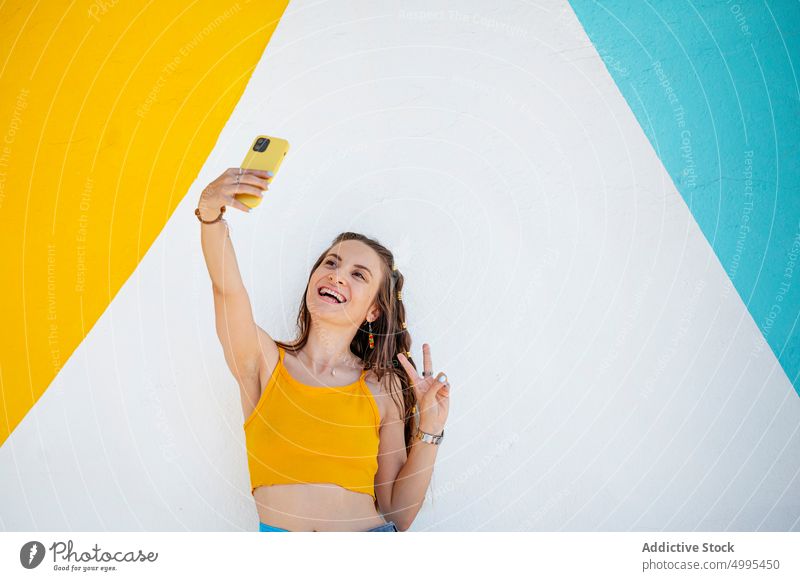 Junge Frau gestikuliert V-Zeichen und nimmt Selfie Lächeln v-Zeichen Smartphone Wand Straße Wochenende Glück hell jung Stil Sommer Funktelefon Apparatur heiter