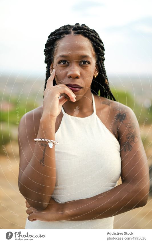Afroamerikanische Frau schaut in der Natur in die Kamera Gesicht berühren Landschaft Sommer Vorschein Stil Porträt Afro-Zöpfe Angebot Erwachsener schwarz