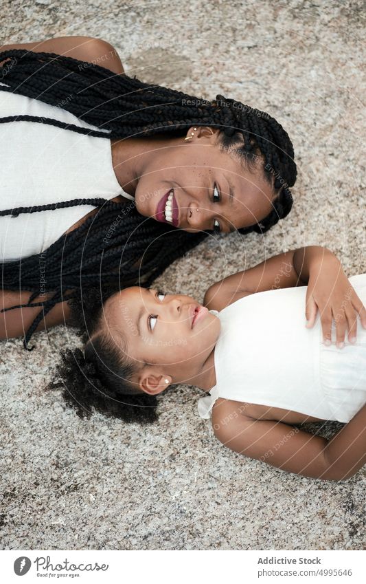 Fröhliche afroamerikanische Mutter und Tochter am Boden Lächeln Glück Menschengruppe Wochenende Zusammensein Liebe Stein Frau Mädchen schwarz Afroamerikaner