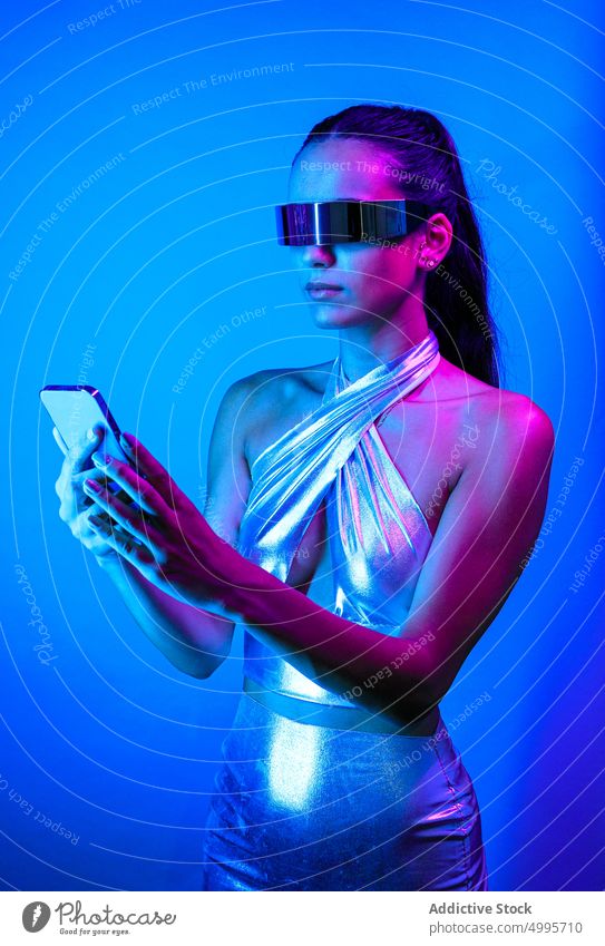 Ernste futuristische Frau am Handy in blauem Studio Virtuelle Realität Smartphone Stil Browsen Erfahrung soziale Netzwerke selbstbewusst VR Cyberspace digital