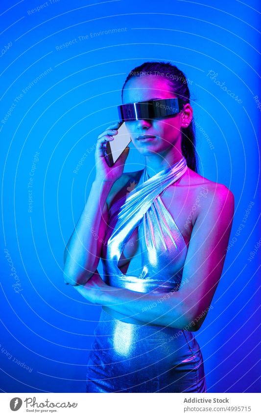 Ernste futuristische Frau, die in einem blauen Studio telefoniert Virtuelle Realität Smartphone Stil Erfahrung selbstbewusst reden VR Kommunizieren Cyberspace