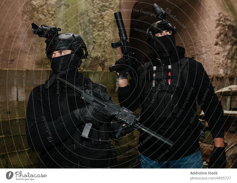 Anonyme Kämpfer mit Gewehren in der Nähe eines schäbigen Gebäudes Männer kämpfen Gefecht zwängen behüten Schlacht gewalttätig Gefahr attackieren Graffiti
