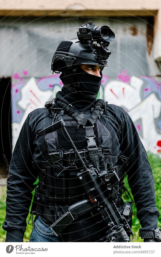 Anonymer Krieger im Schutzanzug, der in der Nähe einer schäbigen Konstruktion wegschaut Mann achtsam ernst Kämpfer Militär Graffiti Waffe selbstbewusst Gefecht