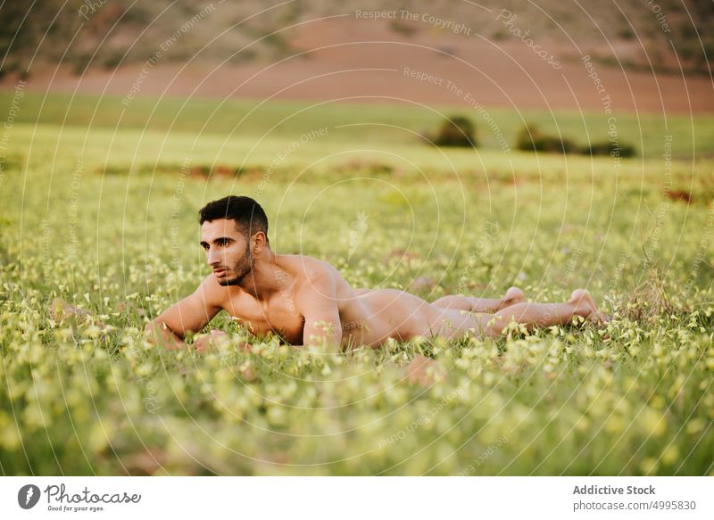 Nackter ethnischer Mann liegt auf einem Feld und schaut weg nackt Lügen Landschaft muskulös Natur selbstsicher Harmonie Erholung Körper selbstbewusst männlich