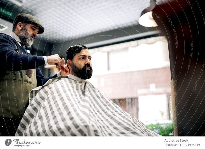 Friseur bürstet das Haar eines Kunden im Salon Klient Kamm Behaarung Frisur Pflege Männer männlich Zusammensein Stil Meister ethnisch hispanisch professionell