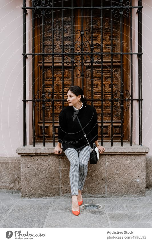 Hispanische Frau sitzt in der Nähe einer Holztür auf der Straße Windstille Großstadt Stil traumhaft feminin Gebäude Persönlichkeit allein verträumt jung