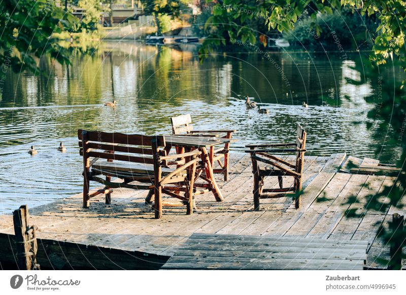 Sitzgruppe aus hölzernen Gartenmöbeln auf einem Steg am See, dahinter Enten Gartenstuhl Holz Brandenburg Terrasse friedlich still sonnig sitzen Bohlen Teich