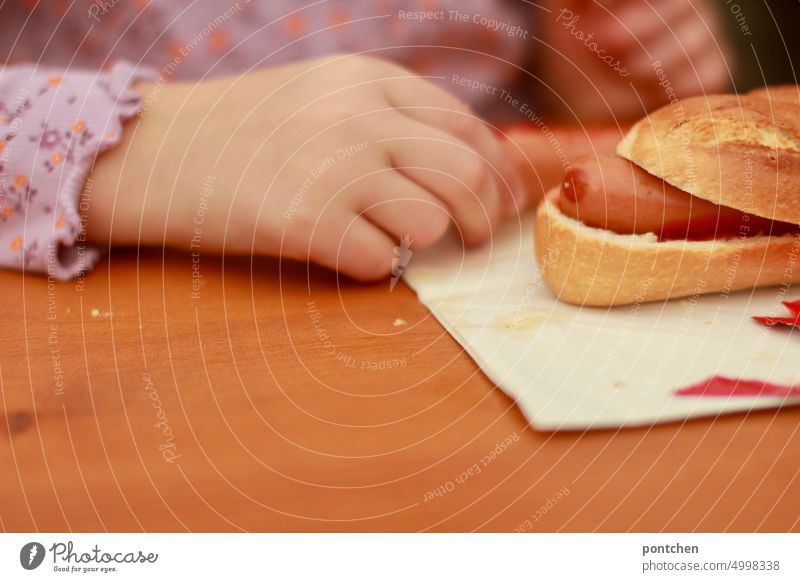 Ein Hotdog liegt auf einem Tisch, biertisch, vor einem Kind. Fastfood essen kind hotdog Ernährung Lebensmittel ungesund Imbiss lecker Appetit & Hunger Snack