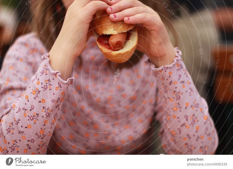 Ein Kind in geblümten Oberteil beißt in einen Hotdog. Fastfood Wienerwurst semmel fastfood essen genuss lecker Mädchen Lebensmittel Ernährung Snack Kleidung
