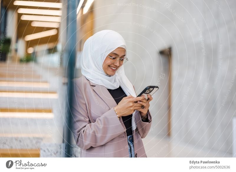 Junge muslimische Frau benutzt ihr Smartphone in einem Haus Thai Schal Hijab Islam islamisch Universität Business Büro echte Menschen jung Erwachsener Schüler