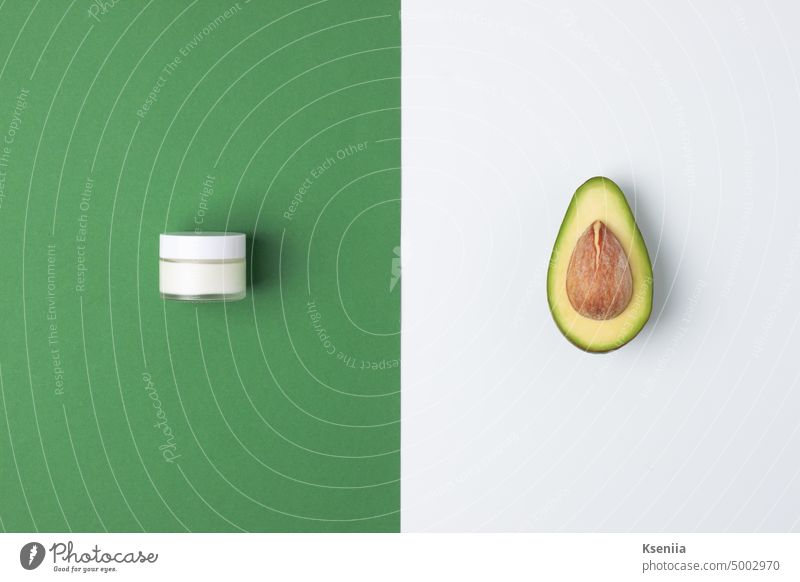 Minimalistische Komposition mit einem Glas Kosmetikcreme und Avocado auf grünem und weißem Hintergrund. Flat lay, copy space Bad Schönheit Körper Körperpflege
