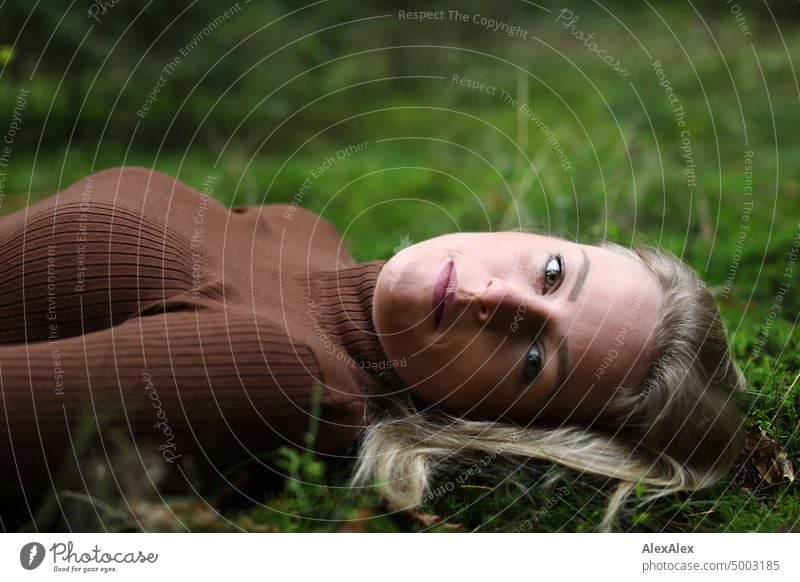 Junge, blonde Frau mit Grübchen liegt im Wald auf dem Moos und schaut von der Seite in die Kamera junge Frau feminin schön glücklich Jugendliche Portrait