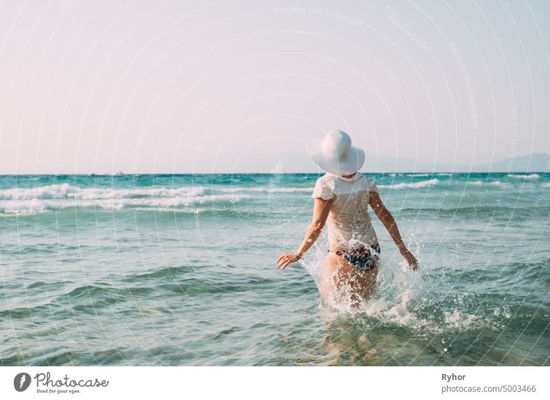 Junge kaukasische Frau Frau in Badeanzug und Sommerhut Walking in Meer. Urlaub am Meer Ozean Strand Ägäis Spritzer aktiv aktiver Lebensstil attraktiv