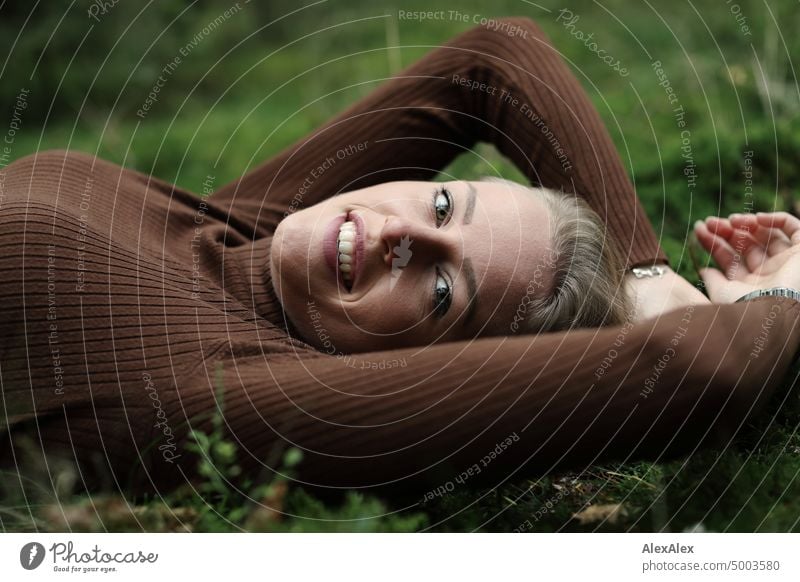 Junge, blonde Frau mit Grübchen liegt im Wald auf dem Moos und lächelt von der Seite in die Kamera junge Frau feminin schön glücklich Jugendliche Portrait