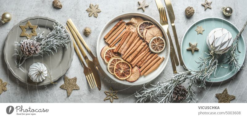 Weihnachtlich gedeckter Tisch mit Tellern, goldenem Besteck, getrockneten Früchten und Wintergewürzen, Weihnachtskugeln und Keksen. Ansicht von oben.