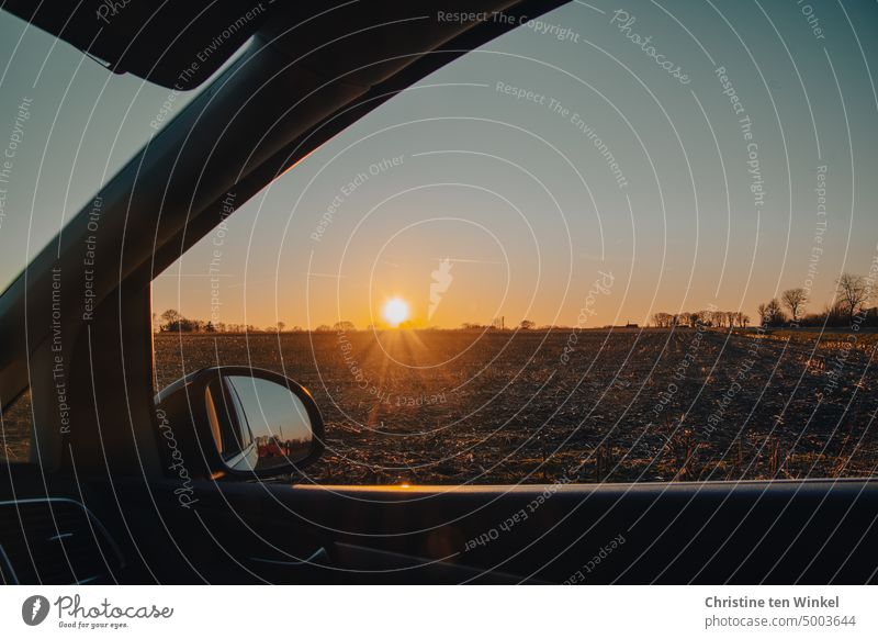 Mit dem Auto am Feldrand stehen und den Sonnenuntergang durch das geöffnete Seitenfenster betrachten Sonnenlicht Sonnenstrahlen Baumreihe Acker schön