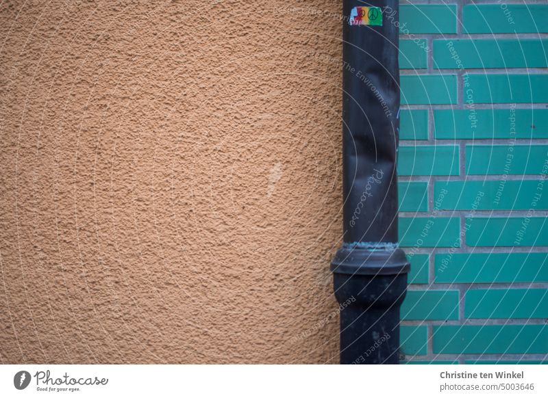 Ein verbeultes Fallrohr mit buntem "Peace" Aufkleber vor einer teils verputzten und teils gefliesten Fassade Peace-Zeichen Gebäude Strukturen & Formen Wand
