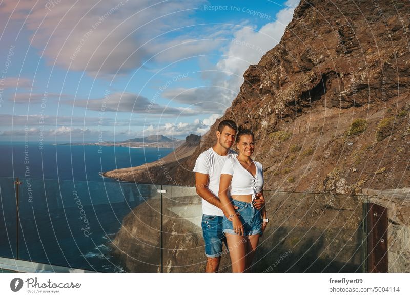 Paar in den Flitterwochen auf einem Aussichtspunkt vor vulkanischen Klippen Liebe jung Kaukasier 20s Sonnenuntergang Kuss Textfreiraum Steine Kanarische Inseln
