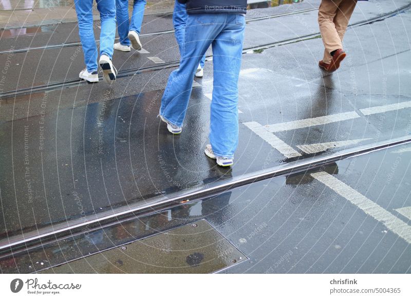 Personen laufen über nasse Straße Regen Gehweg Zebrastreifen Jeans Füße Schuhe Asphalt Strümpfe Beine Ampel Straßenverkehr Verkehr Pfütze Schiene Eisenbahn