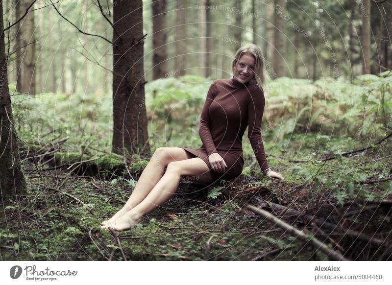 Junge, blonde Frau sitzt barfuß auf einem umgefallenen Baumstamm im Wald und lächelt in die Kamera junge Frau feminin schön glücklich Jugendliche Portrait