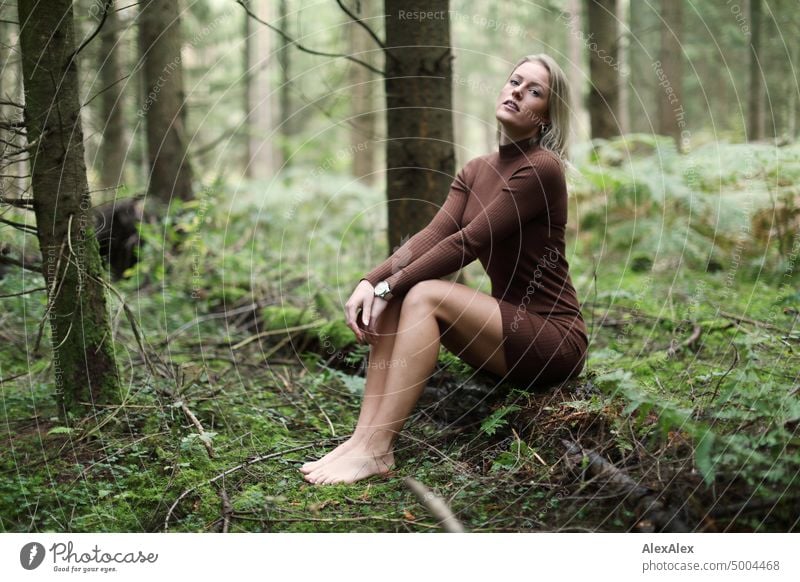 Junge, blonde Frau sitzt barfuß auf einem umgefallenen Baumstamm im Wald und schaut in die Kamera junge Frau feminin schön glücklich Jugendliche Portrait