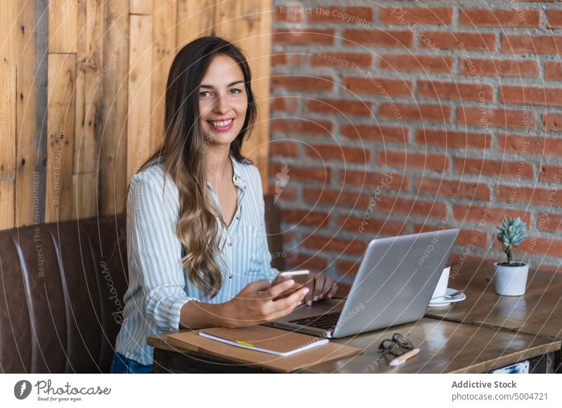 Lächelnde Freiberuflerin mit Laptop in einem Café Geschäftsfrau Frau Smartphone Browsen freiberuflich soziale Netzwerke benutzend Projekt Glück Daten abgelegen