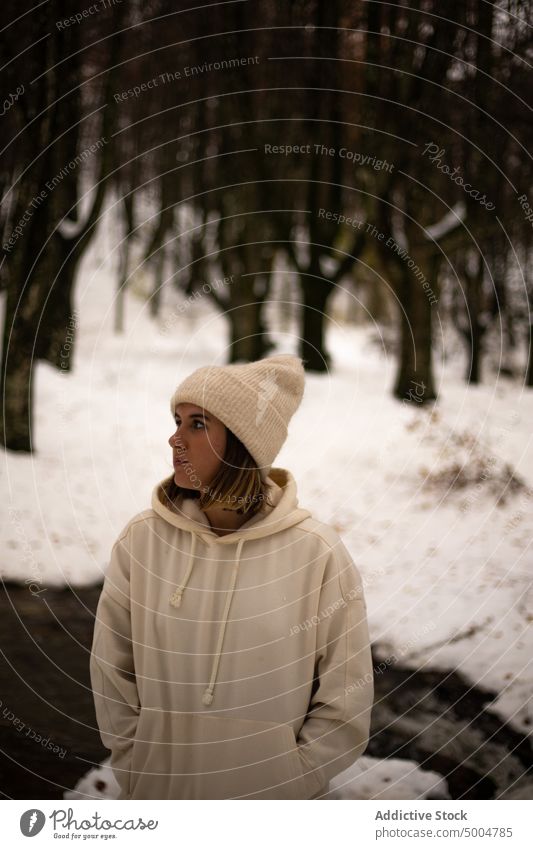 Junge Frau in warmer Kleidung im Winterwald stehend warme Kleidung Schnee kalt verträumt Fluss Wald Winterzeit Natur Wälder Hut Melancholie Hand-in-Tasche
