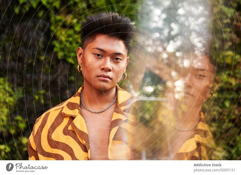 Hübscher nicht-binärer Mann in trendigem Hemd gegen Büsche selbstbewusst Porträt lgbt queer Teint Individualität Gesicht natürliche Schönheit Haut Natur Akne